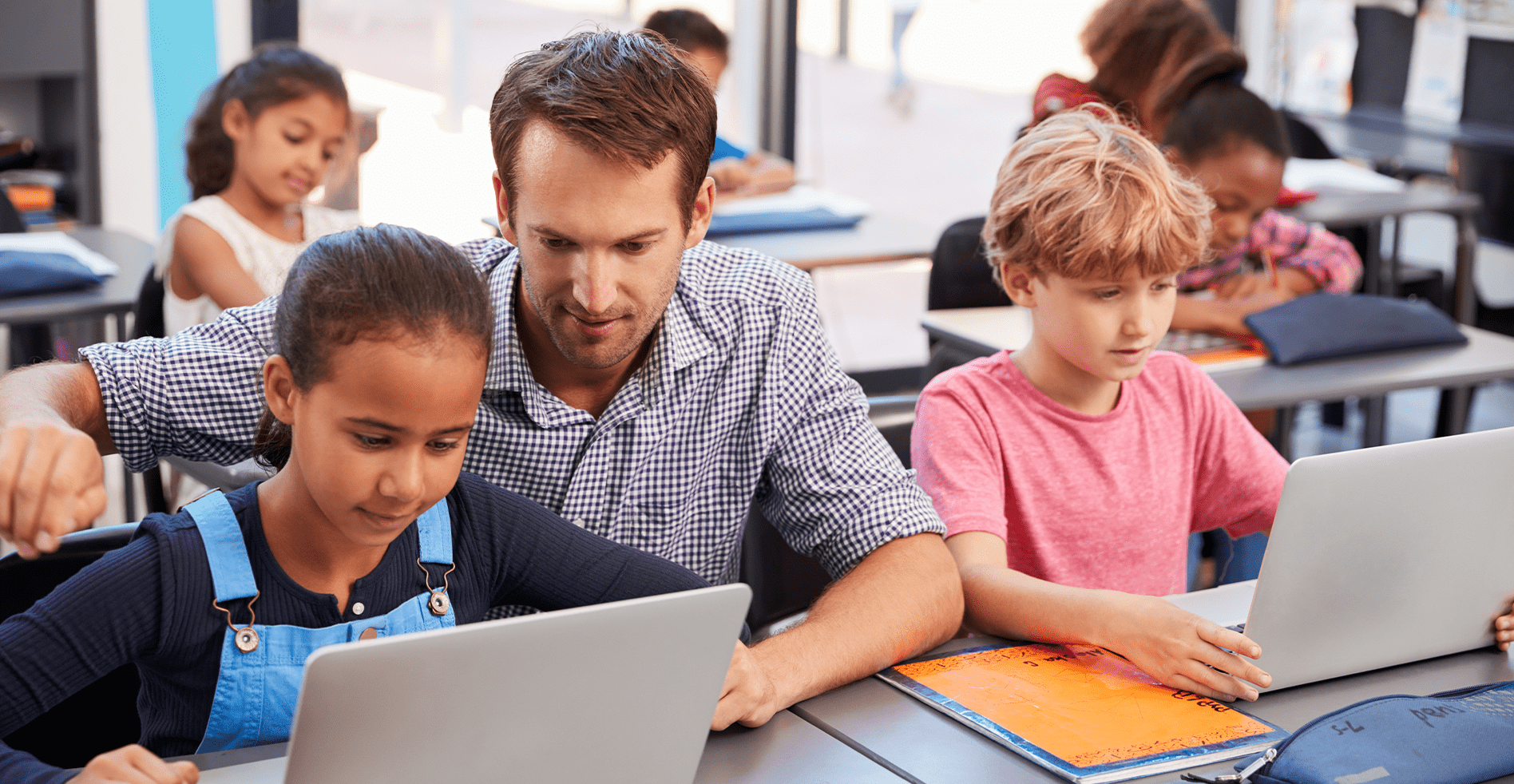 teacher works with students on secure laptops