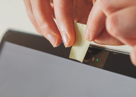 hands cover laptop camera with sticky note